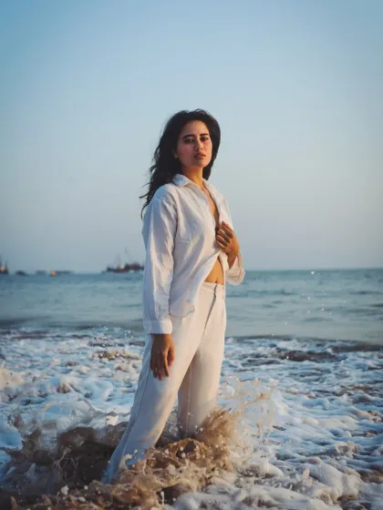 The power of the ocean meets fashion. The waves crashing around the model create a dynamic and energetic scene, highlighting her calm presence amidst the chaos.