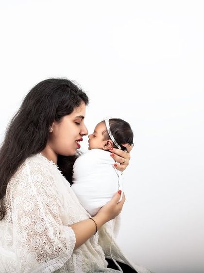 A mother gazes lovingly at her newborn baby. This intimate and simple portrait, set against a white background, is all about their new connection.