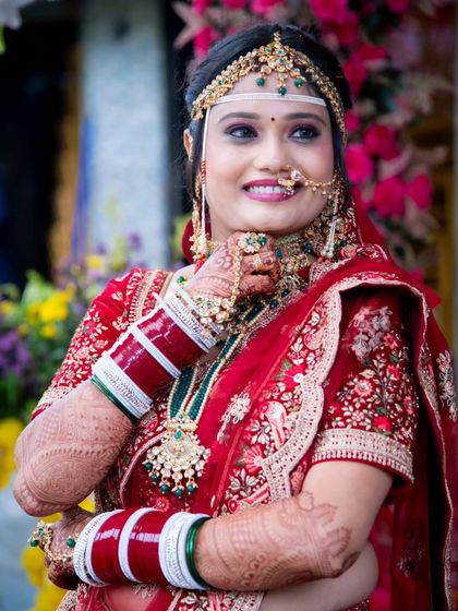 A close-up of the happy bride on her wedding day. This photo beautifully captures her smile, makeup, and the traditional red and green bridal jewellery.