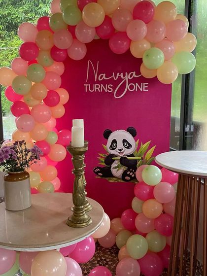 A close-up of the personalized "Navya Turns One" backdrop with a soft-colored balloon arch.