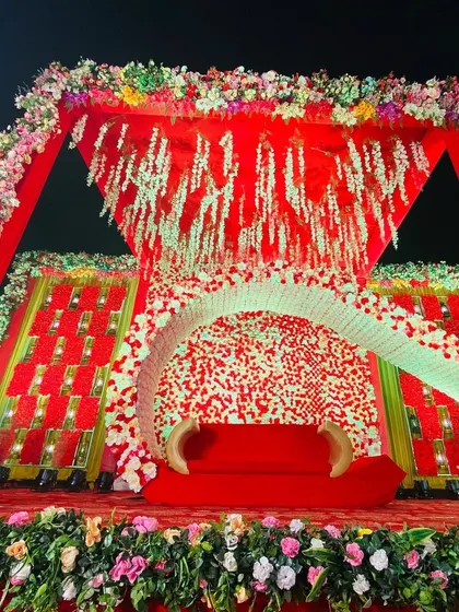 A unique wedding stage design with a large, curved floral element, set against a backdrop of red flowers and hanging wisteria.