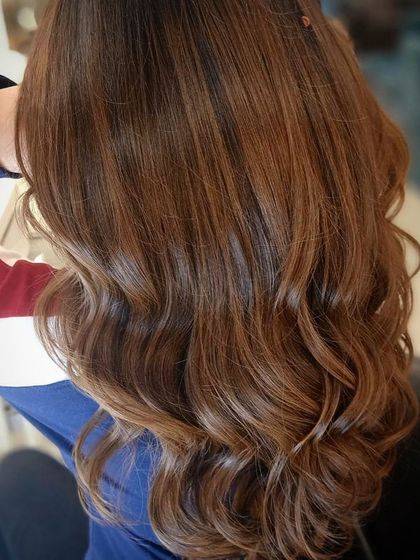 This client's long hair is enhanced with a warm, caramel-toned color, styled into soft waves. The result is a rich and luxurious look that is perfect for any season.