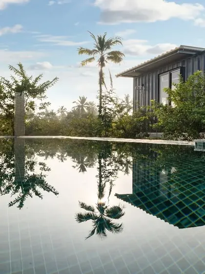 A beautiful shot of a container villa at Suzo Farms, perfectly reflected in the infinity pool. The image captures a moment of perfect calm and luxury, blending modern architecture with a tropical paradise.