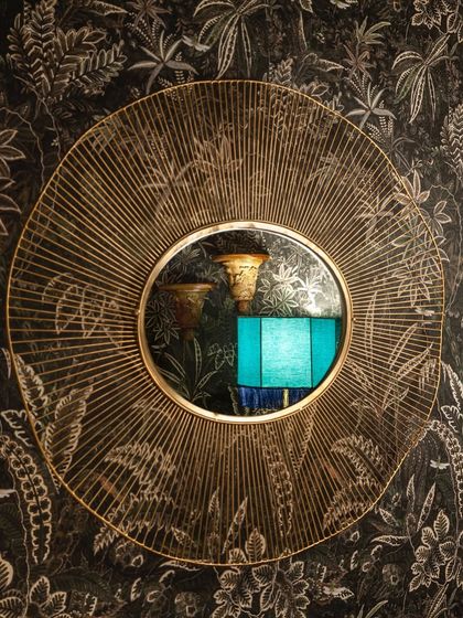 A decorative mirror reflects the unique design elements of our interior, from the custom lamps to the lush, botanical wallpaper.