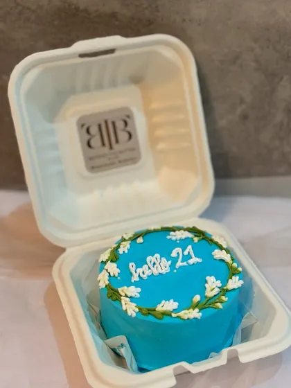 A beautiful blue bento cake for a 21st birthday, decorated with a delicate white floral wreath design and the message "hello 21."