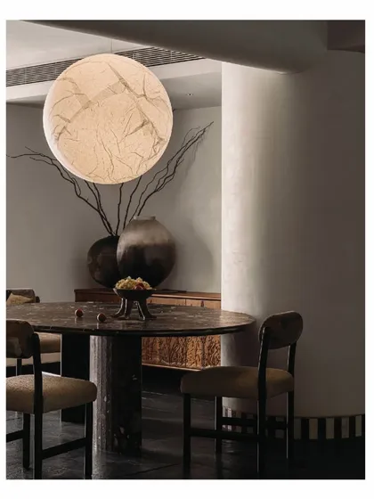 Tucked behind a sculptural wall, the dining area in the 'Aria' home is an intimate space for shared meals. A "Moon" light fixture hangs above the monolithic marble table, creating a dramatic yet serene ambiance that feels both grounded and otherworldly.