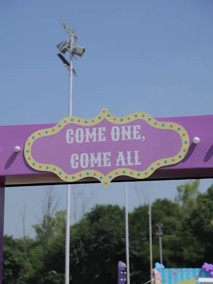 The "Come One, Come All" sign at the entrance of an outdoor carnival, setting the stage for a day of fun and celebration.