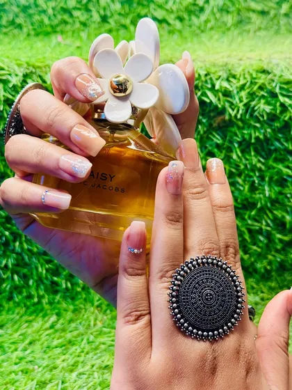 Here, the nude and glitter nail art is paired with a different accessory, showing its versatility. A delicate white floral design is added to one nail for a custom touch.