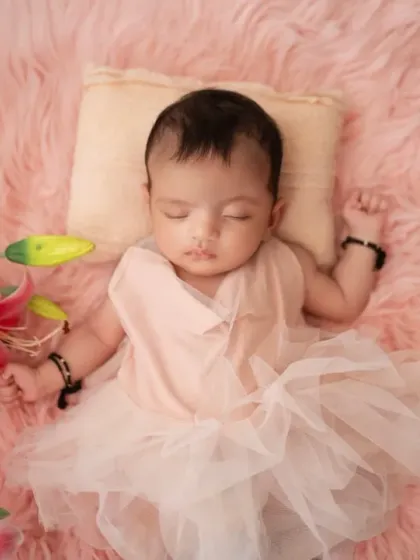 A sleeping newborn in a delicate pink dress, surrounded by fresh pink lilies. We use soft textures and floral elements to create a gentle and feminine aesthetic.