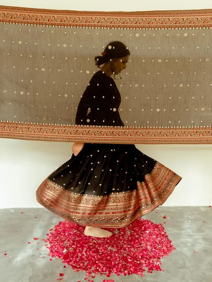An artistic shot for Safaa World, capturing movement as the model spins on a bed of rose petals. The image uses a sheer dupatta to create a sense of layered transparency.