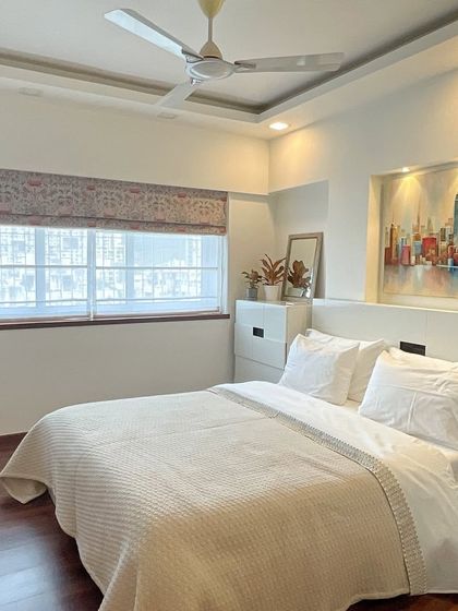 A bright and airy bedroom designed for comfort. The all-white bedding, wooden floors, and large window with sheer blinds create a space that feels clean, calm, and inviting.