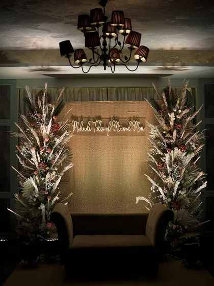 A moody and rustic stage setup for an intimate event, featuring dried pampas grass arrangements and a custom neon sign.