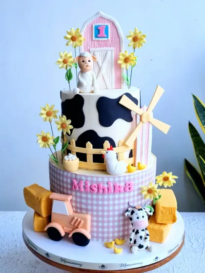 A farm-themed cake perfect for a first birthday. This three-tiered cake features a barn, a windmill, and adorable fondant animals like a sheep, cow, and chicken.