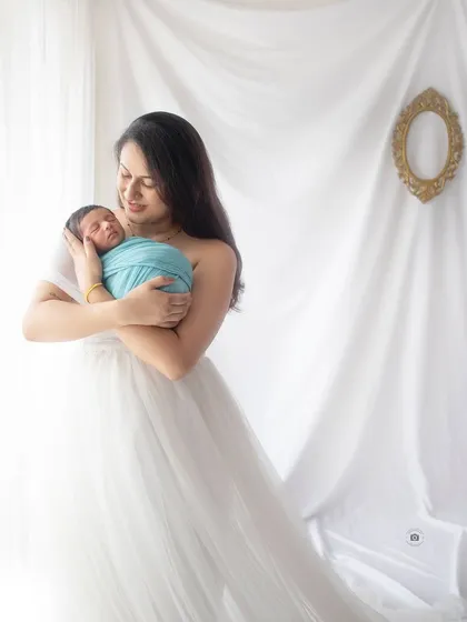 A serene portrait of a new mother holding her baby. The soft white dress and bright, airy background give this newborn photo a timeless and angelic feel.