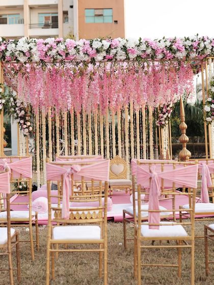A beautiful pink and gold mandap for a day wedding. The design features hanging pink wisteria, golden pillars, and elegant seating for a classic, romantic ceremony.