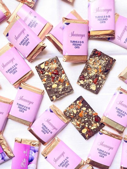 Celebrating a special birthday with custom chocolate bars. These mini chocolates, wrapped in personalized pink sleeves for Shanaya's party, are perfect as party favors.