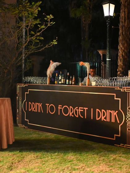 An outdoor bar setup for the Gatsby party. The custom-built bar front with its period-appropriate font and design, along with professional bartenders, added an authentic touch to the celebration.