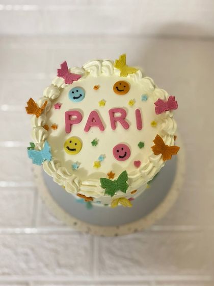 A top-down view of this cheerful vanilla cake, decorated with colourful smilies and butterflies for Pari.