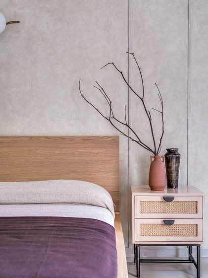 A detail shot of the autumnal master bedroom, focusing on the contrast between the dark wood, the cane nightstand, and the textured wall. The dried branches add a sculptural, natural element.