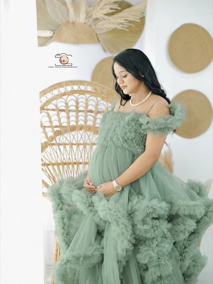 A serene side-profile portrait of the mother-to-be in a ruffled green gown. Seated in a wicker chair, she looks down at her bump, creating a moment of quiet reflection.