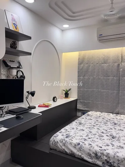 A full view of a compact bedroom that doubles as a workspace. The bed is integrated with a desk and storage unit, featuring an arched niche and floating shelves to maximize functionality without sacrificing style.