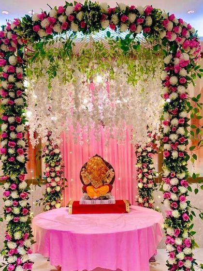A beautiful floral archway for Ganpati, decorated with pink and white roses and hanging white wisteria. This design creates a heavenly entrance for Bappa, perfect for home celebrations.