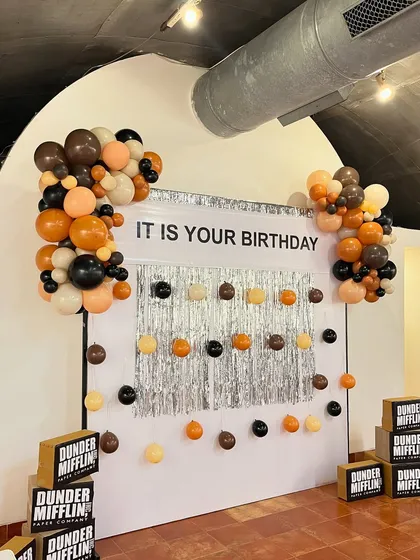 Another angle of the main party backdrop, showing the balloon garlands in a muted, office-appropriate color palette of browns, beiges, and black. The entire setup was designed to be instantly recognizable to fans.
