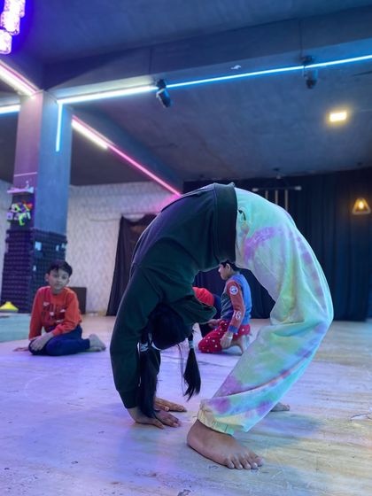 A young gymnast holds a strong backbend position on the floor. This exercise is crucial for developing spinal flexibility and shoulder strength needed for tumbling and acrobatics.