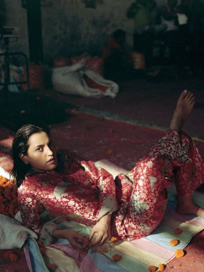 A full-length shot capturing a relaxed pose amidst the flower market. The styling of the printed co-ord set against the colorful floor mat and piles of flowers creates a grounded, yet highly fashionable, composition.