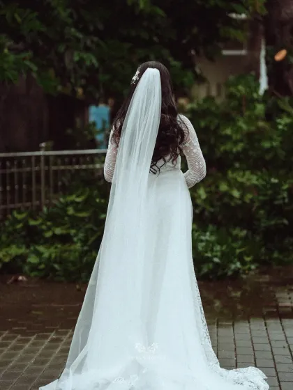 A view from behind, showcasing the elegant flow of the bride's veil and the detailed lacework of her gown as she walks.
