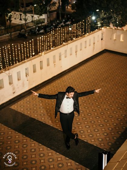 The groom striking a pose on a terrace decorated with string lights, a fun reception shot.