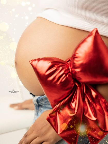 A close-up shot focusing on the baby bump as the ultimate Christmas gift, complete with a shiny red bow. This is a creative and memorable idea for a holiday-themed shoot.