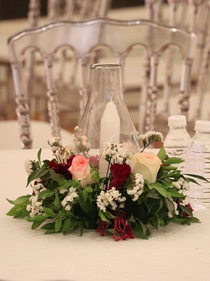 A simple yet beautiful table centerpiece featuring a candle in a glass hurricane lamp, surrounded by a wreath of fresh red and white flowers.