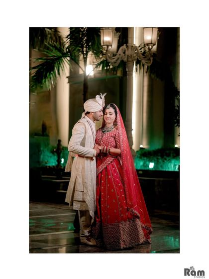 An intimate night-time portrait of the groom kissing his bride's forehead, with elegant lamps and palm trees creating a romantic, resort-like feel.