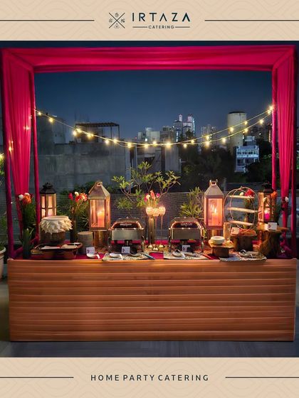 A vibrant home party catering setup with a pink draped backdrop and string lights, perfect for a lively celebration on a terrace or balcony.