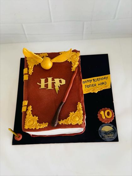 A cake designed to look like a magical spellbook from the world of Harry Potter, complete with a wand and golden snitch.