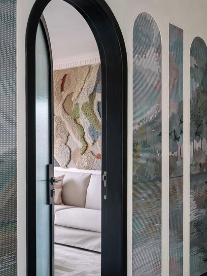 A view through an arched doorway into the home office lounge, highlighting the large textural tapestry and unique arched wall panels.