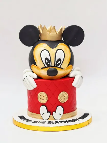 A sculpted Mickey Mouse cake, where Mickey is peeking over the side. A fun and creative design for any Disney fan.