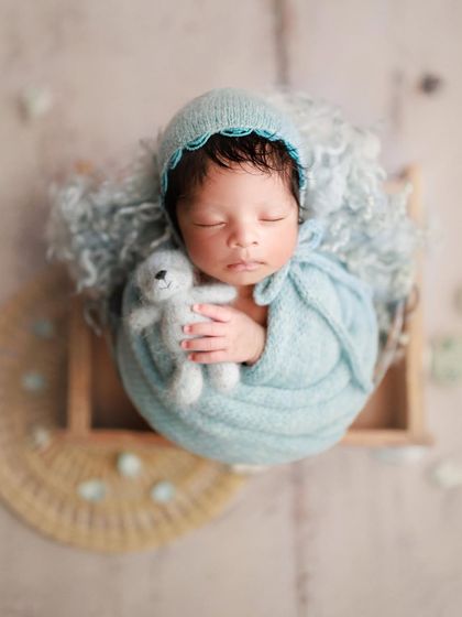 A precious bundle of love. This overhead shot in a wooden box highlights the beautiful textures of the blue wrap and the tiny teddy bear.