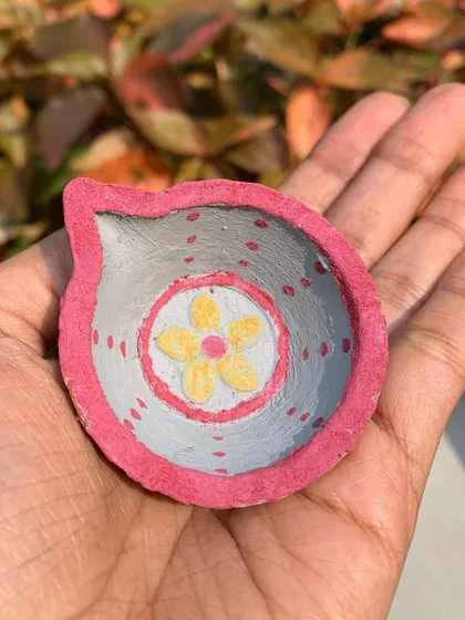 A single hand-painted diya resting in my palm. The simple dot and flower motif is created with natural clay paints, making it an eco-friendly and beautiful decorative item.