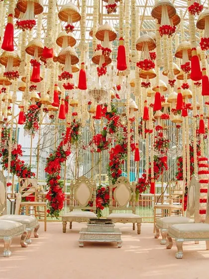 A breathtaking mandap decorated with hanging red tassels, temple bells, and strings of white flowers. The design is a beautiful tribute to traditional Indian craftsmanship and festive colors.