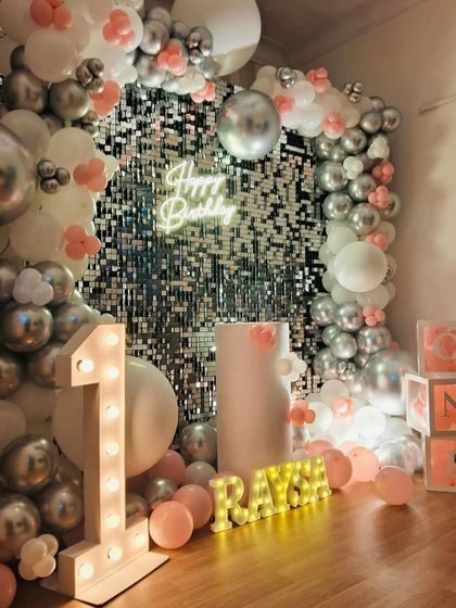 A first birthday is a huge milestone. We created this stunning photo corner with a silver sequin wall, a pink, white, and silver balloon arrangement, and light-up letters and numbers for baby Raya's special day.