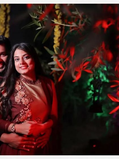A vibrant couple portrait taken at night. The red floral background adds a pop of color and romance, beautifully framing the couple in their elegant attire.