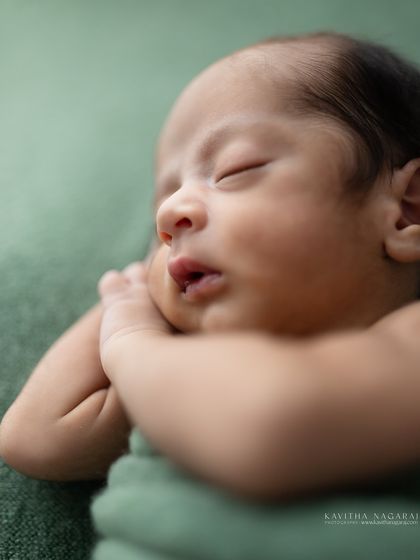 A nine-day-old newborn in a classic curled-up pose. The soft light and simple green wrap create a serene and timeless portrait.
