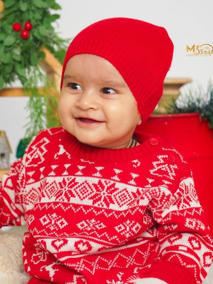 A sweet close-up of the baby in a festive red sweater. His bright, happy smile is the perfect centerpiece for a holiday photo.