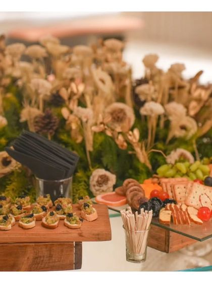 A section of a grazing table featuring olive tapenade bruschetta and a cheese board, set against a backdrop of dried floral arrangements. We coordinate our food styling with the event's overall decor theme.