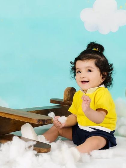 A happy baby boy sits among the clouds with a toy airplane and a globe, ready to travel the world.
