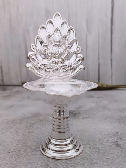 A simple yet elegant German silver diya with a lotus backplate featuring Goddess Lakshmi. It's a beautiful piece for your daily pooja.