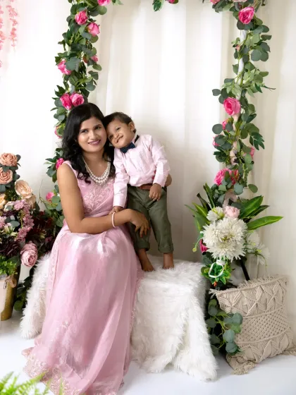 A mother and her son pose by the floral arch, the little boy standing on the seat and leaning affectionately on his mom.