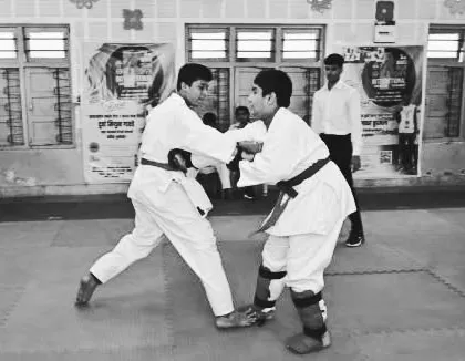 Two male students demonstrate their kumite skills under the watchful eye of a referee. The belt exam evaluates both technical proficiency and fighting spirit.